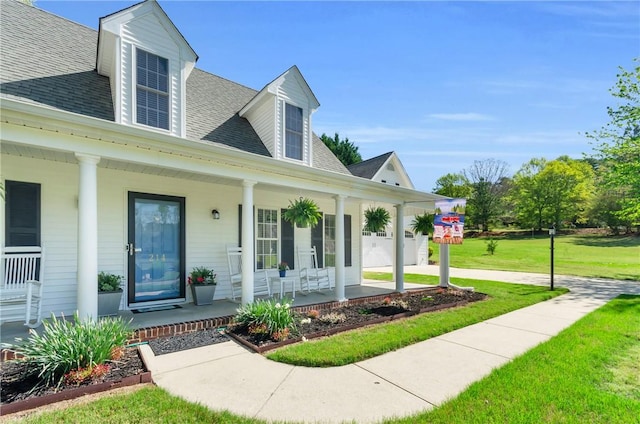 view of front of house with a front lawn, covered porch, a garage, and roof with shingles
