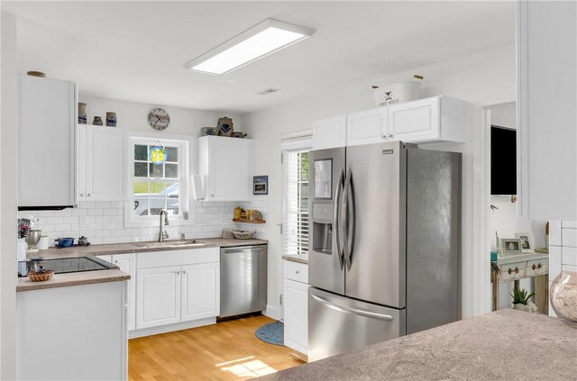 kitchen featuring tasteful backsplash, white cabinets, a sink, light wood finished floors, and stainless steel appliances