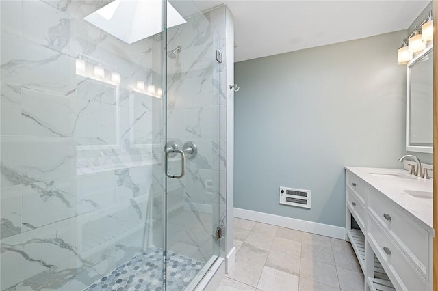 bathroom featuring a marble finish shower, a sink, double vanity, baseboards, and a skylight