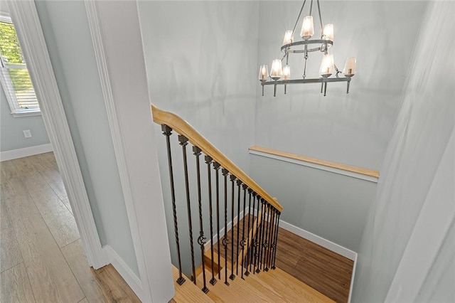stairway with an inviting chandelier, wood finished floors, and baseboards