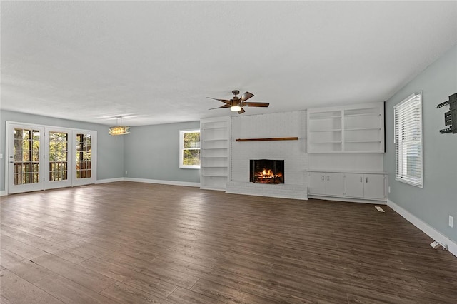 unfurnished living room with ceiling fan with notable chandelier, baseboards, a fireplace, and a healthy amount of sunlight