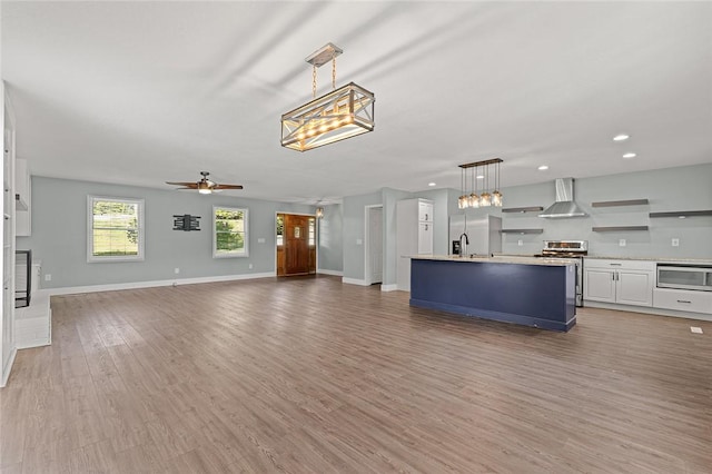 kitchen with hanging light fixtures, stainless steel appliances, light wood finished floors, light countertops, and wall chimney exhaust hood