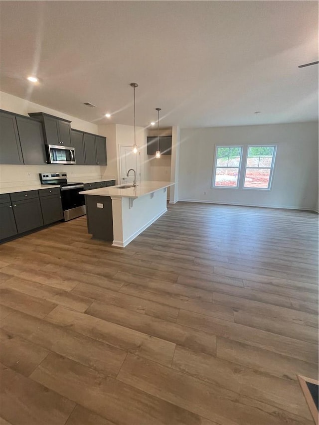 kitchen with wood finished floors, a center island with sink, appliances with stainless steel finishes, open floor plan, and a breakfast bar area