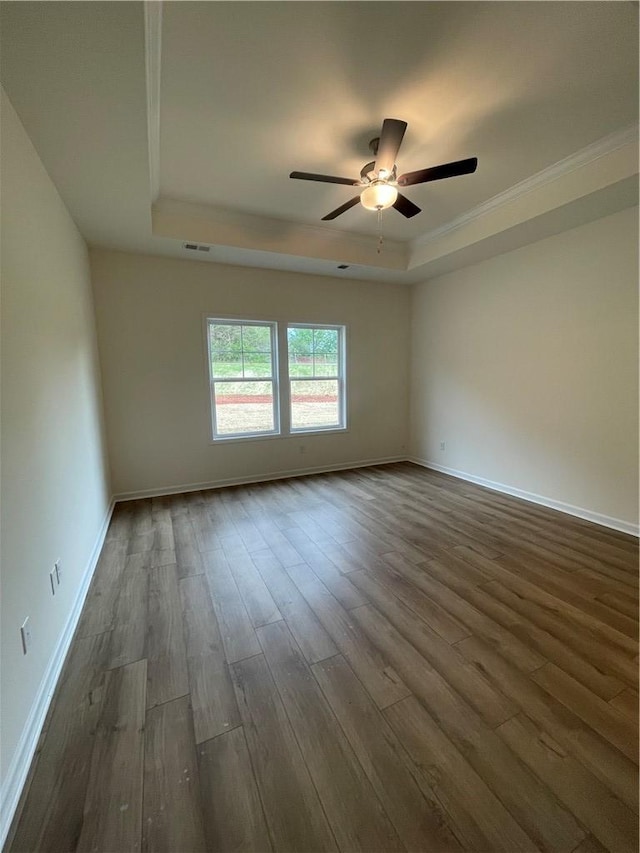 empty room featuring dark wood-style flooring, baseboards, ceiling fan, crown molding, and a raised ceiling
