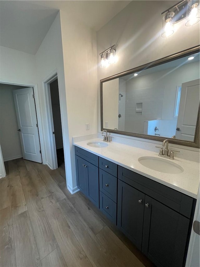 bathroom with wood finished floors, a sink, double vanity, and tiled shower
