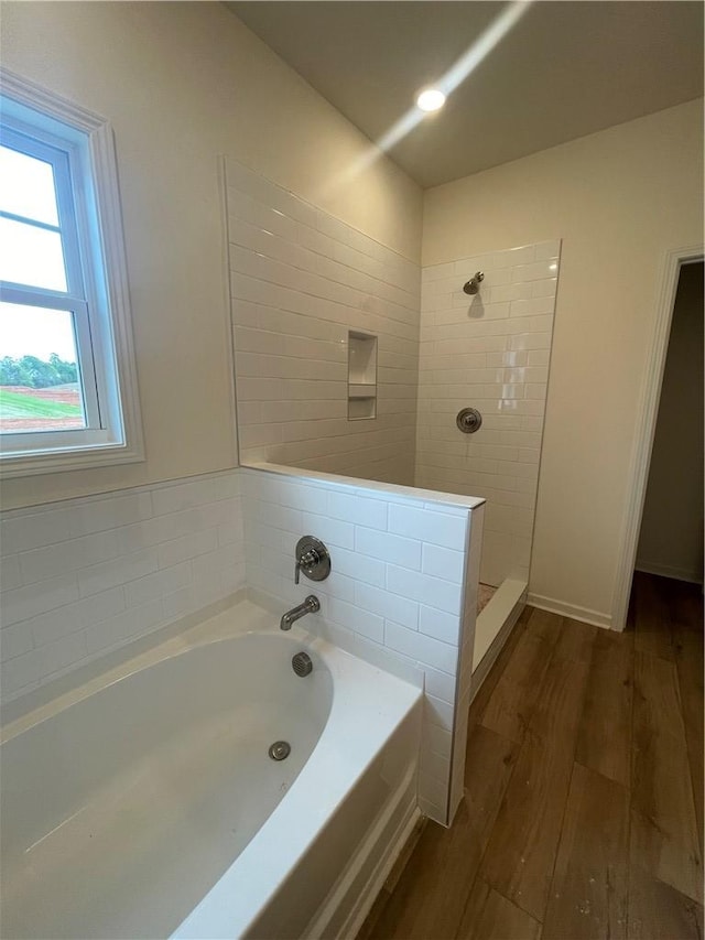 bathroom featuring a bath, wood finished floors, and tiled shower