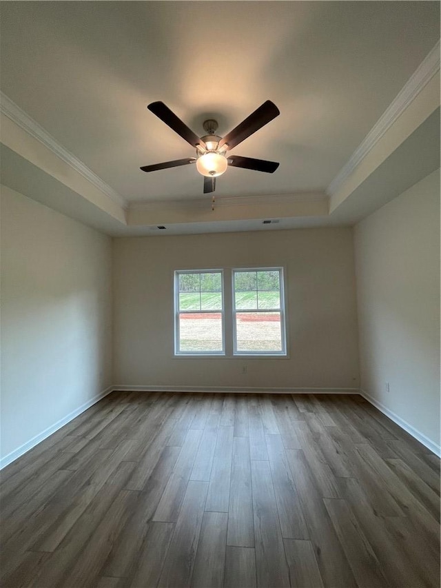 empty room with a tray ceiling, ornamental molding, and dark wood finished floors