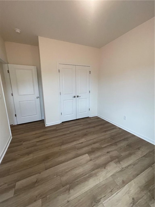 unfurnished bedroom featuring baseboards, wood finished floors, and a closet