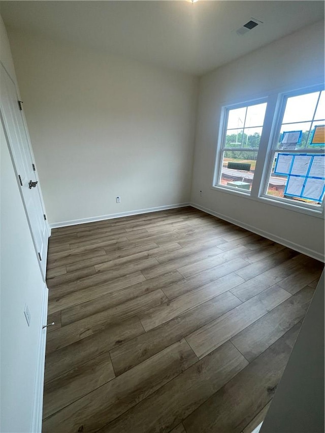 empty room featuring baseboards, wood finished floors, and visible vents
