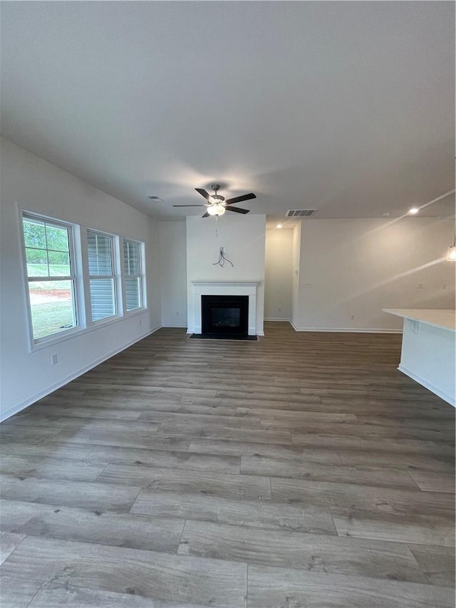 unfurnished living room featuring visible vents, a glass covered fireplace, baseboards, a ceiling fan, and wood finished floors