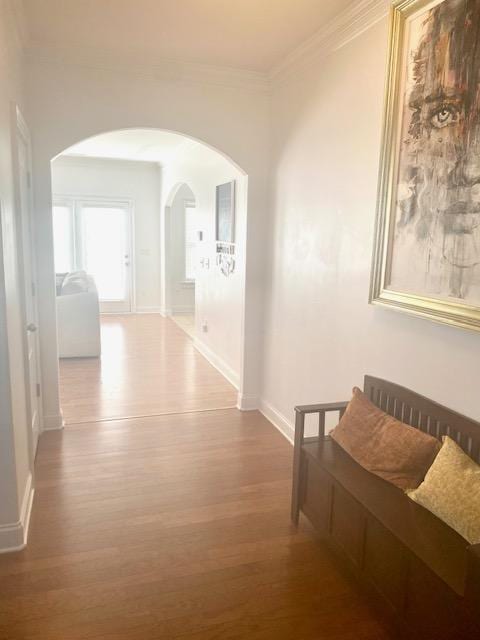 hall featuring baseboards, wood finished floors, arched walkways, and ornamental molding