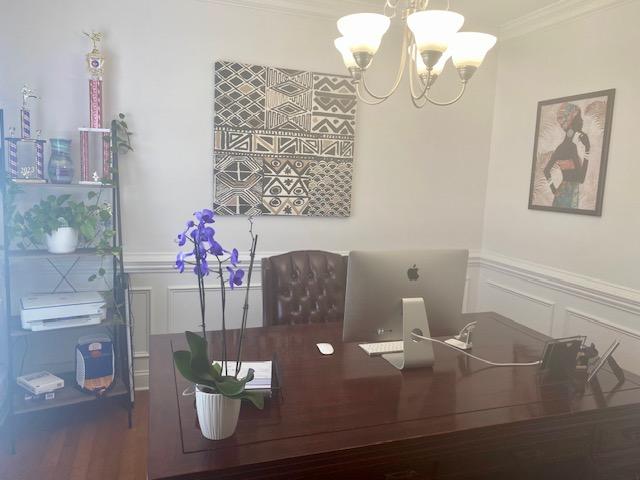dining space featuring a decorative wall, crown molding, wood finished floors, wainscoting, and an inviting chandelier