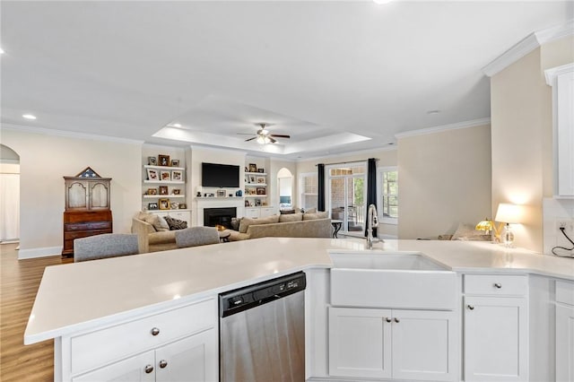 kitchen with light countertops, a warm lit fireplace, a ceiling fan, stainless steel dishwasher, and a sink