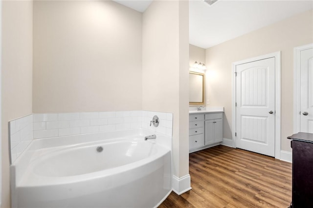 full bathroom featuring wood finished floors, baseboards, a garden tub, and vanity
