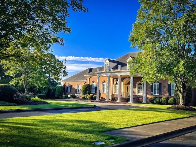 greek revival house with brick siding, a front lawn, and covered porch