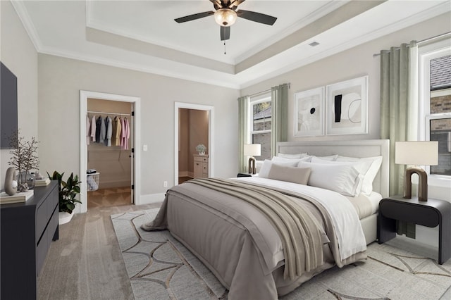 bedroom with a raised ceiling, connected bathroom, a walk in closet, crown molding, and light colored carpet