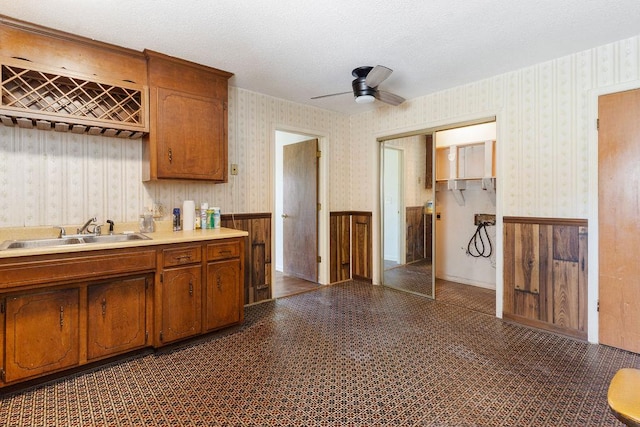 221 Lakeview Dr, Liberty, SC 29657 - kitchen with a ceiling fan, a sink, wallpapered walls, wainscoting, and brown cabinets