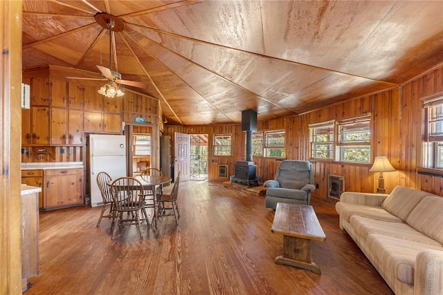 living area with wooden walls, wood finished floors, a wood stove, vaulted ceiling, and wooden ceiling