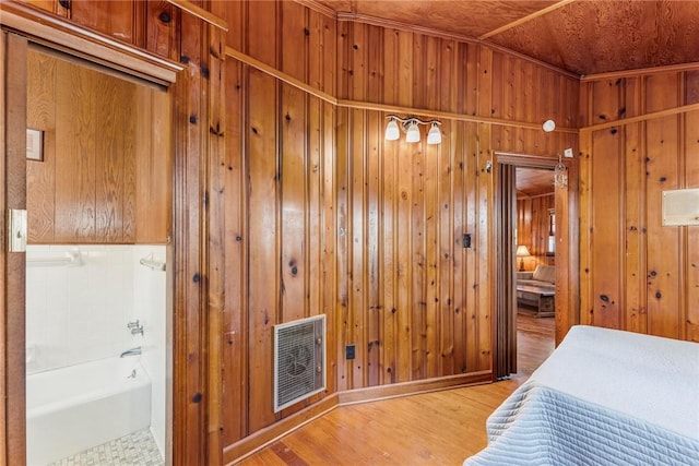 bedroom with light wood finished floors, wood walls, and visible vents