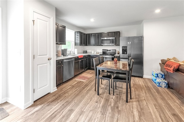 kitchen featuring a sink, stainless steel appliances, baseboards, light wood-style floors, and dark cabinetry