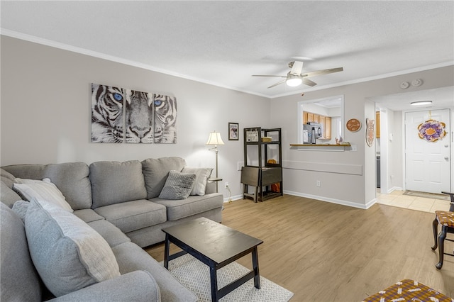 living area featuring light wood-type flooring, ornamental molding, baseboards, and ceiling fan