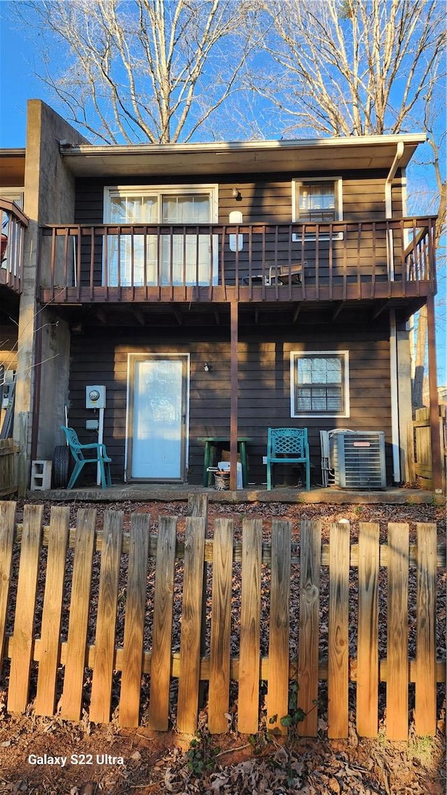 rear view of property featuring a fenced front yard, central air condition unit, and a balcony