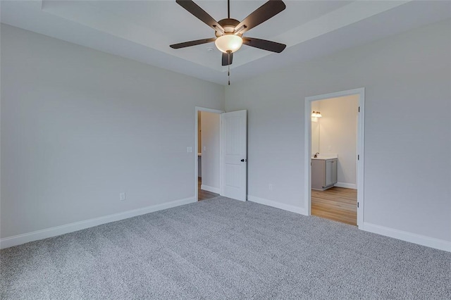 unfurnished bedroom featuring carpet flooring, baseboards, connected bathroom, a tray ceiling, and ceiling fan