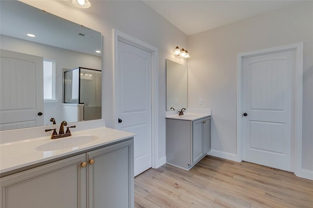 full bath with wood finished floors, two vanities, a stall shower, and baseboards