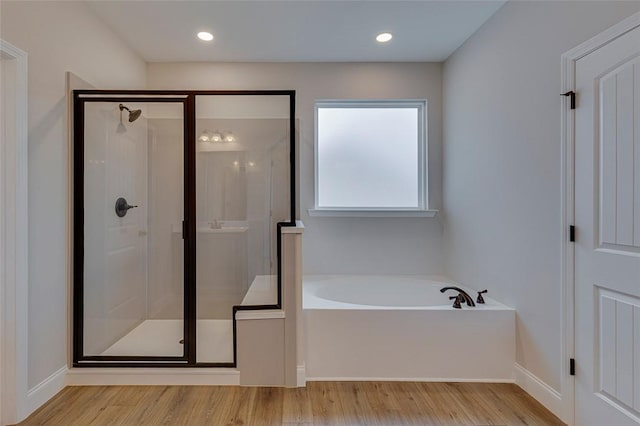 bathroom with a garden tub, a stall shower, wood finished floors, and baseboards
