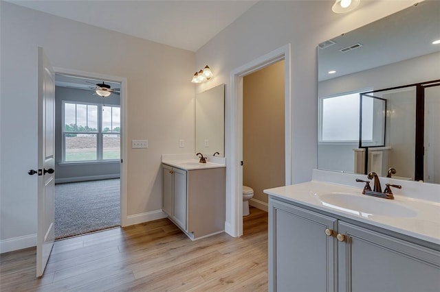 bathroom with wood finished floors, toilet, two vanities, baseboards, and ceiling fan