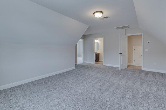 additional living space featuring vaulted ceiling, light colored carpet, and baseboards