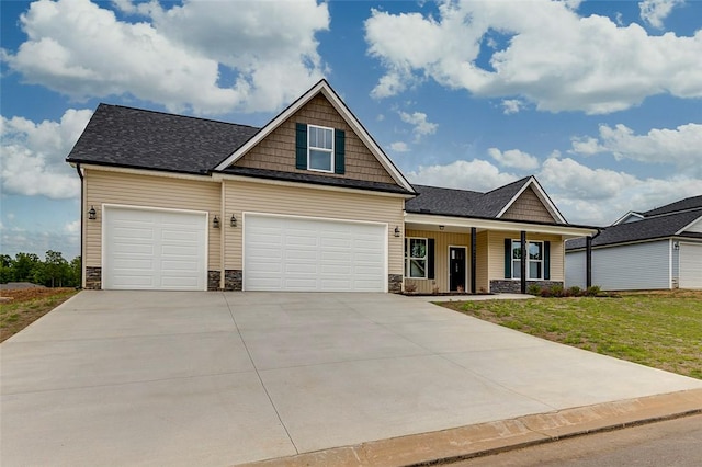 craftsman-style home with stone siding, concrete driveway, a front lawn, covered porch, and roof with shingles