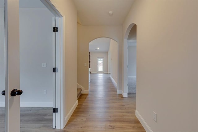 hallway with arched walkways, light wood-type flooring, baseboards, and stairway