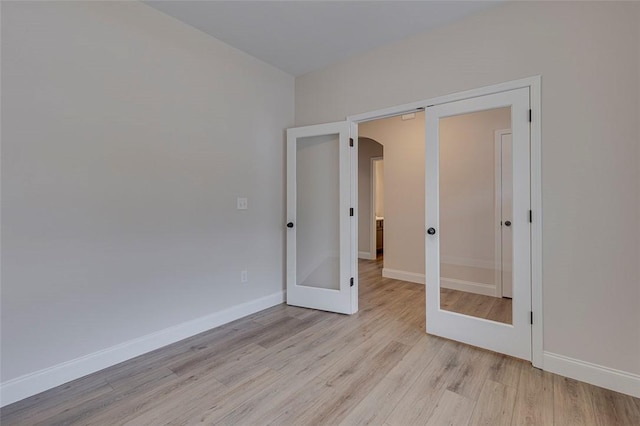 unfurnished bedroom with arched walkways, light wood-type flooring, french doors, and baseboards