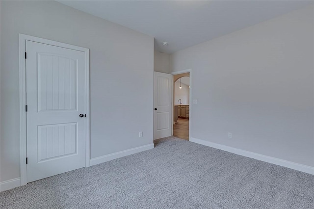 unfurnished bedroom featuring carpet, baseboards, and arched walkways