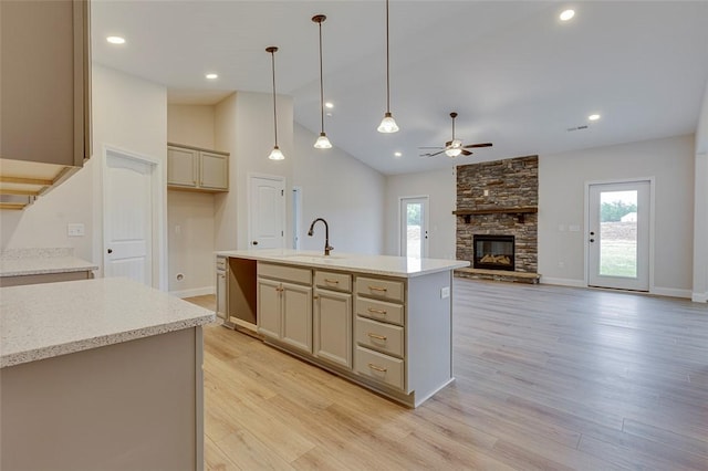kitchen featuring a sink, ceiling fan, a fireplace, light wood-style flooring, and pendant lighting