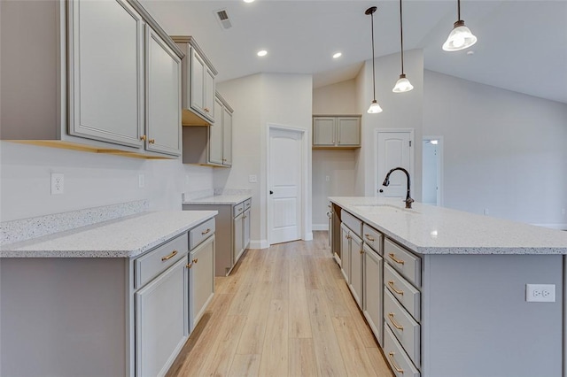 kitchen featuring gray cabinets, a sink, a center island with sink, light wood finished floors, and vaulted ceiling