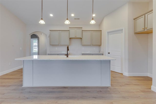 kitchen featuring a sink, arched walkways, baseboards, a kitchen island with sink, and recessed lighting
