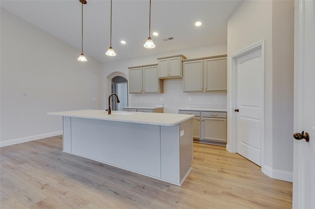 kitchen featuring a sink, arched walkways, baseboards, a kitchen island with sink, and recessed lighting