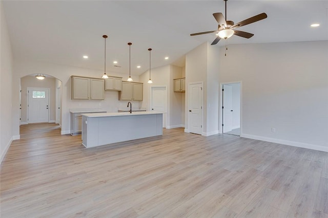 kitchen featuring baseboards, arched walkways, ceiling fan, a center island with sink, and light countertops