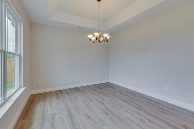 unfurnished room with light wood-style floors, a chandelier, a tray ceiling, and baseboards