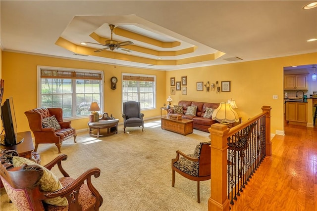 living room featuring a tray ceiling, crown molding, baseboards, and a ceiling fan
