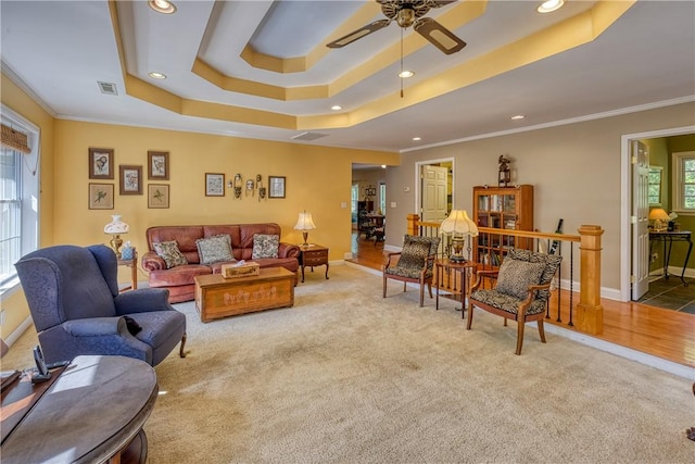 carpeted living room featuring a tray ceiling, visible vents, ornamental molding, and ceiling fan