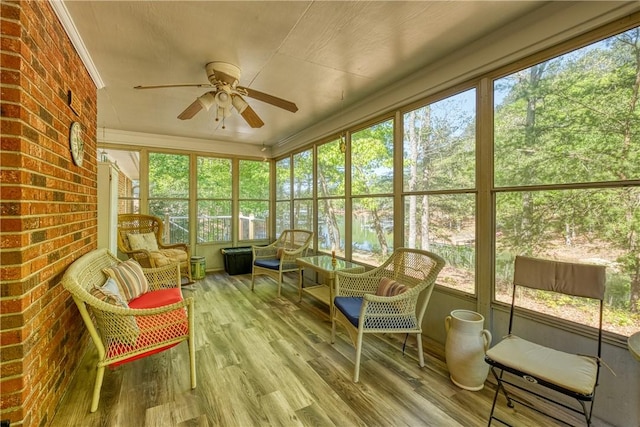 sunroom with plenty of natural light, a ceiling fan, and a water view