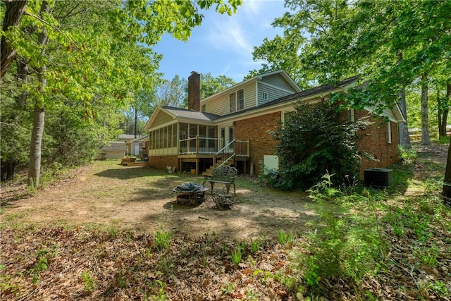 rear view of house featuring central AC, brick siding, a chimney, an outdoor fire pit, and a sunroom