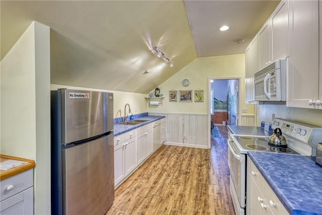 kitchen with a sink, wainscoting, white appliances, white cabinets, and lofted ceiling