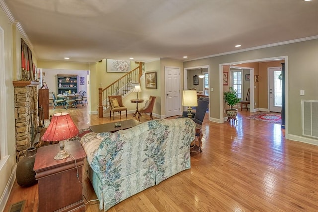 living room with wood finished floors, visible vents, crown molding, and stairs