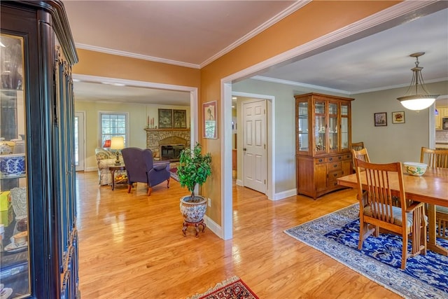 dining space featuring a glass covered fireplace, light wood-type flooring, baseboards, and ornamental molding