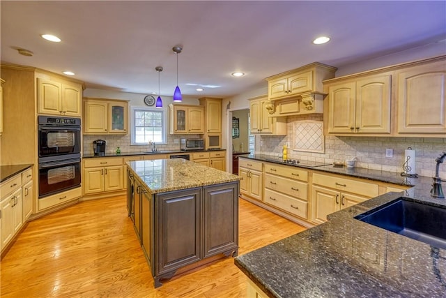 kitchen featuring light wood finished floors, light brown cabinets, glass insert cabinets, black appliances, and tasteful backsplash