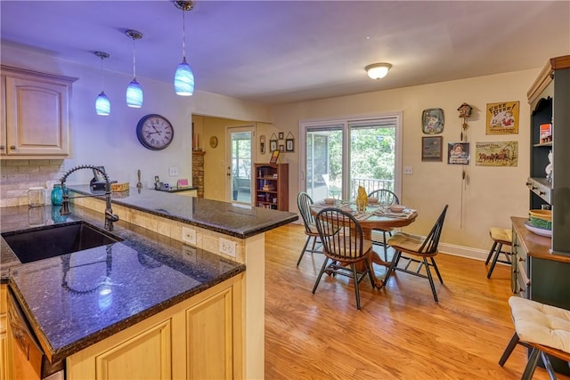 kitchen with dark stone countertops, a sink, light wood-style flooring, decorative light fixtures, and a peninsula